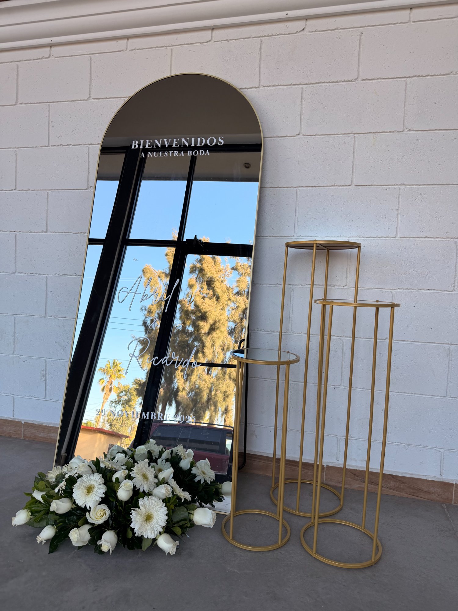 Espejo Personalizado Premium de Verde y Menta Eventos — espejo oscuro personalizado con texto Abril y Ricardo, bases doradas y arreglo de flores blancas para boda